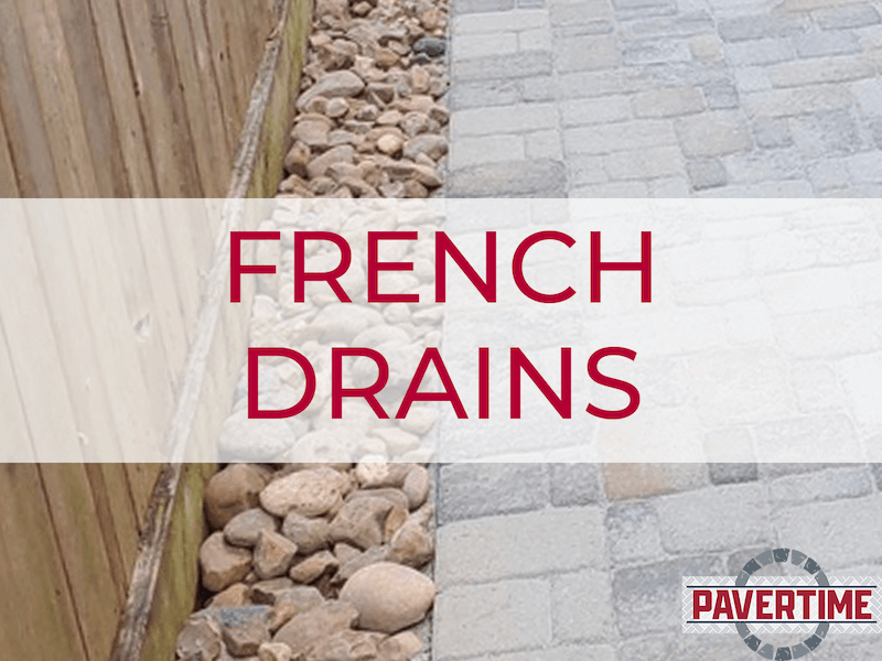 Linear drain covered with rocks alongside a wooden fence next to a paved patio supported by Pavertime