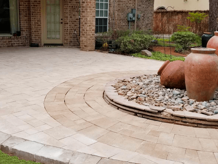 Circular concrete paver patio with two colors around a set of large olla jars on a rock bed.
