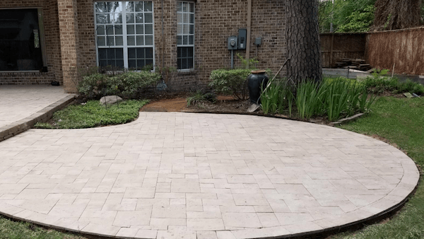 Circular concrete paver patio with multi-size patten surrounded by green plants.